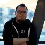 Roberth Strand, standing in front of a window, wearing a Kubernetes hoodie and his company t-shirt